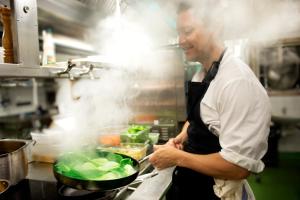 a man in a kitchen preparing food in a wok at Åkerblads Hotell Gästgiveri Spa in Tällberg