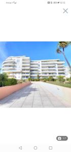 a large white apartment building with a palm tree at Iago lodge azur, 5 minutes à pied de la plage in Fréjus