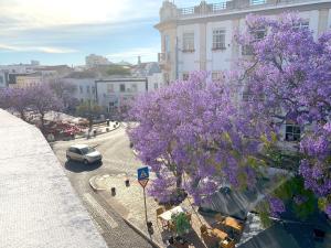 a street with purple trees and a car on a road at The Central Guesthouse in Faro