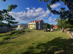 a large house on a grassy field with a tree at Apartmani Mamić in Tomislavgrad