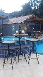 two tables and chairs next to a swimming pool at Pousada Recanto da Cascata in Águas de Lindóia