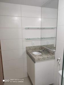 Baño blanco con lavabo y espejo en Confortável Flat com piscina de borda infinita na cobertura, en Cabedelo
