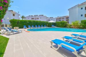 a swimming pool with blue lounge chairs next to a building at Apartamentos Llevant in Port de Pollensa