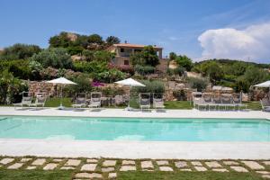 a swimming pool with chairs and umbrellas and a house at La Corte Di Pulicinu in Baja Sardinia
