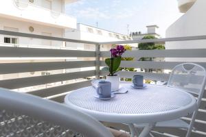 een witte tafel met twee kopjes en paarse bloemen op een balkon bij Casa Plauto in Bellaria-Igea Marina