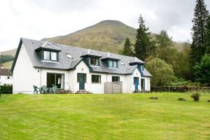 a white house with a mountain in the background at Capercaillie Cottage in Crianlarich