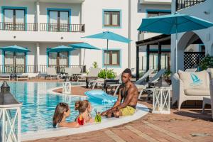 un hombre y dos niños sentados en la piscina en un resort en Hotel La Funtana en Santa Teresa Gallura