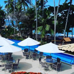 een groep tafels en stoelen met parasols naast een zwembad bij Enseada Praia do Forte in Praia do Forte
