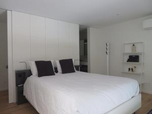 a white bedroom with a large white bed with black pillows at Les Ecuries - Triplex contemporain avec jardin in Avignon