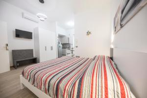 a white bedroom with a bed with a striped blanket at Trinacria Apartments in Cefalù