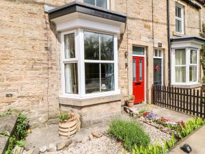 a brick house with a red door and a fence at Hawthorne Cottage in Barnard Castle