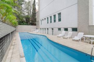 una piscina con sillas, una mesa y un edificio en Vossa Bossa Pinheiros Style, en São Paulo
