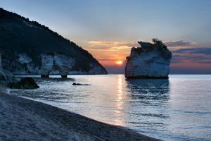 un tramonto su una spiaggia con rocce in acqua di AH Premium Baia dei Faraglioni a Mattinata