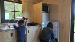 two people in a wooden kitchen with a sink at Lacustra Cabanes accessibles en canoé et Chalets tout confort in Flayat