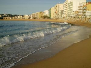 a beach with buildings and the ocean and waves at Pensió Costa Brava in Sant Antoni de Calonge