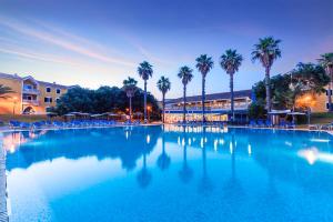 a large swimming pool with palm trees and a hotel at Vibra Blanc Palace Aparthotel in Sa Caleta