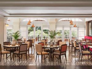 a dining room with tables and chairs and windows at Raffles Hotel Le Royal in Phnom Penh