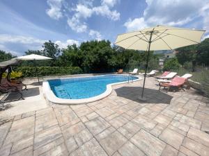 a swimming pool with an umbrella and chairs and a table at Apartmani Matković in Jadranovo