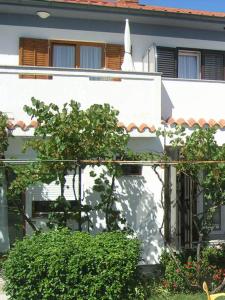 ein weißes Gebäude mit Bäumen und Büschen davor in der Unterkunft Apartments Jadranka with magnificent views of the sea - Baska in Baška