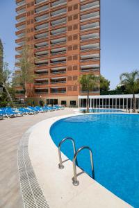 a swimming pool with chairs and a tall building at Aparthotel BCL Levante Lux in Benidorm