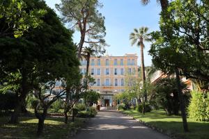 a building in the middle of a park with palm trees at Hôtel Miléade L'Orangeraie - Menton in Menton