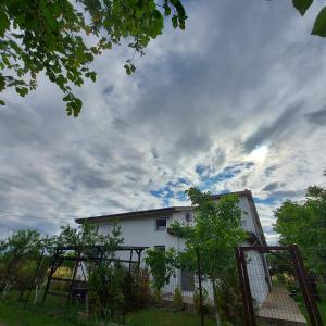 a white house behind a fence with a cloudy sky at Villa Romelia - Select Apartments in Vadu