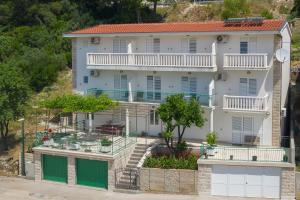 een groot wit gebouw met groene deuren en bomen bij Apartmani Petracie in Drvenik