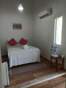 1 dormitorio con 1 cama blanca con almohadas rojas y ventilador en Hospedaria Dedo de Moça en Praia do Espelho