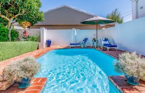a swimming pool with an umbrella and chairs in a backyard at Bleu Cobalt Cottage in Franschhoek