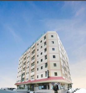 Al Rayan Hotel في عجمان: مبنى ابيض كبير فيه سيارات تقف امامه