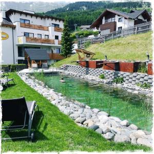 Un río con rocas en la hierba junto a un edificio en Hotel Garni Alpendiamant, en Fiss