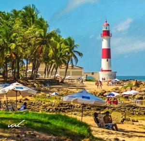 a lighthouse on a beach with people sitting under umbrellas at Apartamentos Itapuã Residence - Praia in Salvador