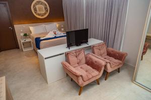 a hotel room with a bed and a tv and two chairs at Nova Onda Hotel in Cabo Frio