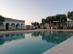 a swimming pool with palm trees and a building at Hacienda Soto-Hego Haizea in Chiclana de la Frontera