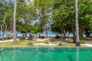 a swimming pool in front of a beach with trees at Amahelia Luxury Resort & Restaurant - Gili Asahan in Gili Asahan