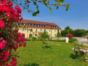 a building with red flowers in front of a yard at Hotel Dvorac Jurjevec in Lekenik