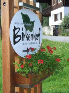 a sign for a restaurant with flowers in a planter at Birkenhof in Sankt Veit in Defereggen