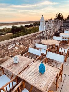eine Terrasse mit Tischen, Stühlen und einem Sonnenschirm in der Unterkunft Forte De Sao Joao Da Barra in Cabanas de Tavira