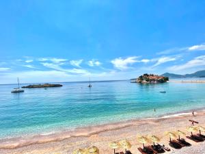 a beach with umbrellas and the blue water at Plava Vila Beach Apartments Sveti Stefan in Sveti Stefan