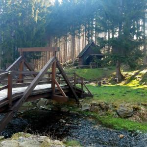 a bridge over a stream with a cabin in the background at Gray House Apartmán in Zlaté Hory