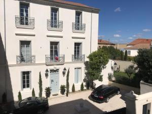 a white building with two cars parked in front of it at LAZARE Maison de Maître , appartements de standing avec parking privatif à seulement 7 minutes à pied du centre historique de Béziers in Béziers