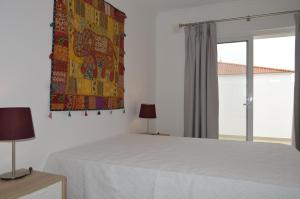 um quarto com uma cama branca e uma janela em Moradia V2 nova e próximo da praia em Vila Nova de Cacela