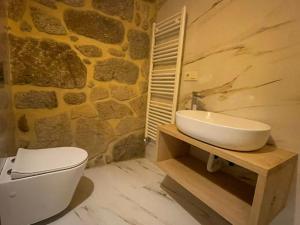 a bathroom with a sink and a toilet and a stone wall at CASA DA ESCOLA in Lobios