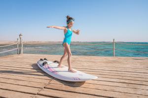 a young girl standing on a surfboard on a pier at Amwaj Beach Club Abu Soma in Hurghada