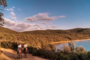 two people riding horses on a dirt road next to a river at Marina di Scarlino Resort in Puntone di Scarlino