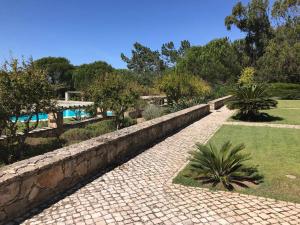 a stone retaining wall next to a garden with a pool at Villa Malveira in Alcabideche