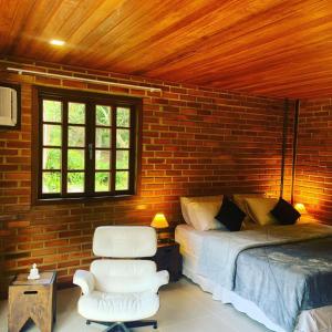 a bedroom with a bed and a chair and a brick wall at Cactus Chalé em lumiar in Lumiar