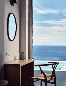 a bathroom with a mirror and a chair next to a window at Etheria Luxury Villas & Suites in Agios Nikolaos