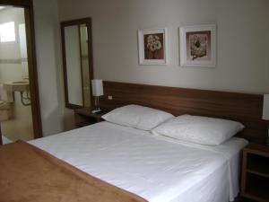 a bedroom with a white bed with a wooden headboard at Hotel Areias Brancas in Rosário do Sul