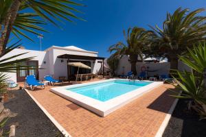 a swimming pool with blue chairs and a house at Villas Reina in Costa Teguise